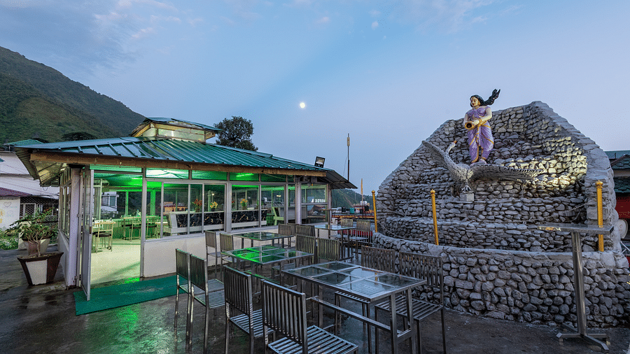 A view of an outdoor dining area at a resort with a stone fountain and a statue in the foreground -  DLS Meghavan Resort